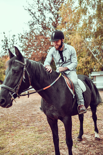 Smiling Male Jockey Petting Horse During Ranch Training Session