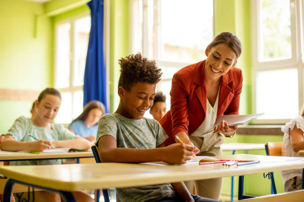 istock Young boy is sitting in classroom, consulting with teacher. 1327279732