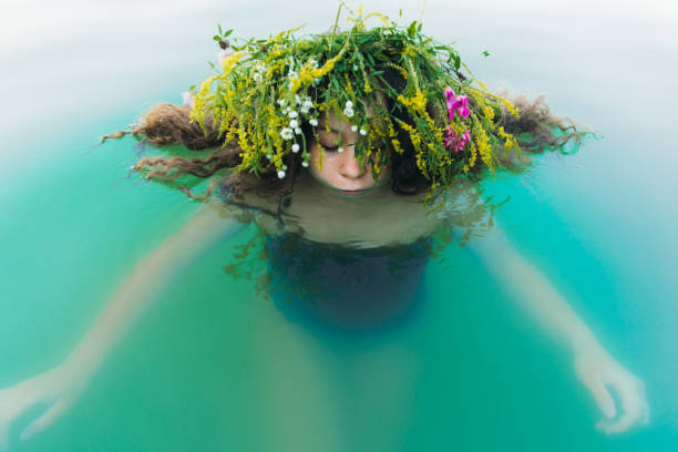 giovane donna che indossa ghirlade di fiori nuotando nel lago durante l'estate kupala night - splashing color image front view head and shoulders foto e immagini stock