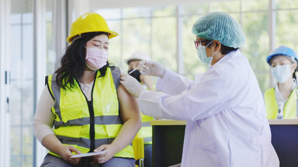 COVID-19 Vaccination station in construction industry. Doctor are vaccinating to group engineer worker protect COVID-19 or flu in hospital. People wear face mask protection from virus. health welfare stock photo