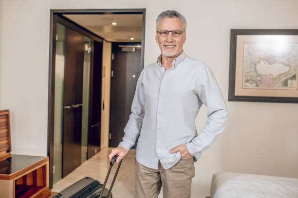 istock Gray-haired confident man with a suitcase in a hotel room 1327285799