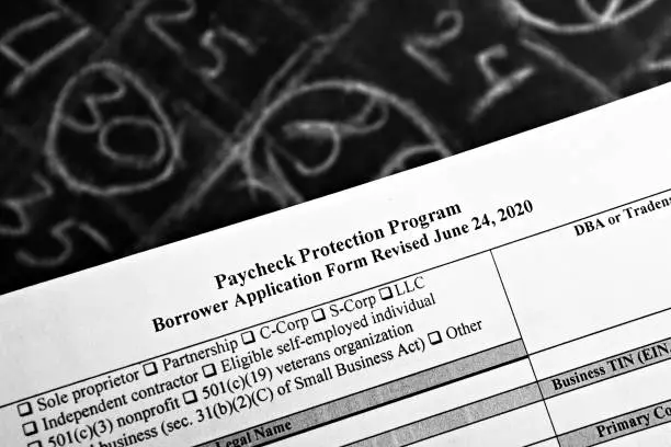 Photo of selective focus monochrome photo of paycheck protection program borrower application form revised, on a background of chalk board with numbers