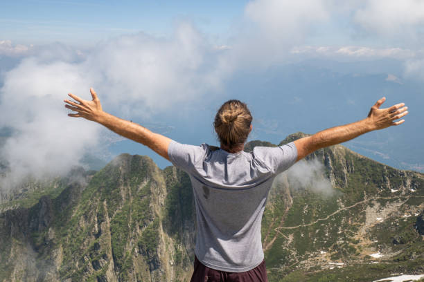 istock Young man on mountain top stands arms outstretched 1327294301