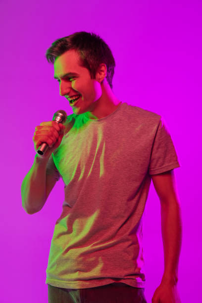 istock One young smiling handsome guy with microphone isolated over pink neon background. Concept of facial expression and human emotions 1327298391