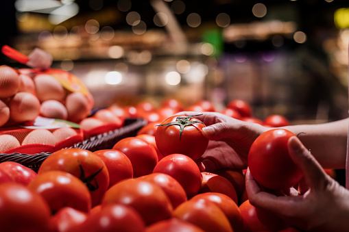 Cropped shot of young asian woman shopping for fresh organic tomatoes in supermarket.Zero waste concept