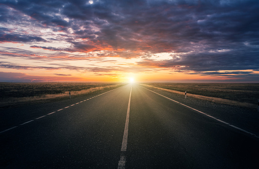 Dramatic sky, cloudy landscape and sunset in the steppe over the highway illuminated by the rays of the setting sun