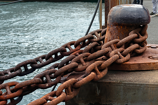 Stud link type rusty ship anchor chain and one headed mooring bitt on a ferry port.