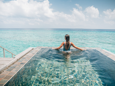 Woman enjoying tropical vacations in an infinity pool in private over water villa. People travel luxury holidays