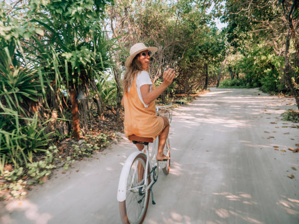 istock Young woman riding bicycle on white sand island 1327303875