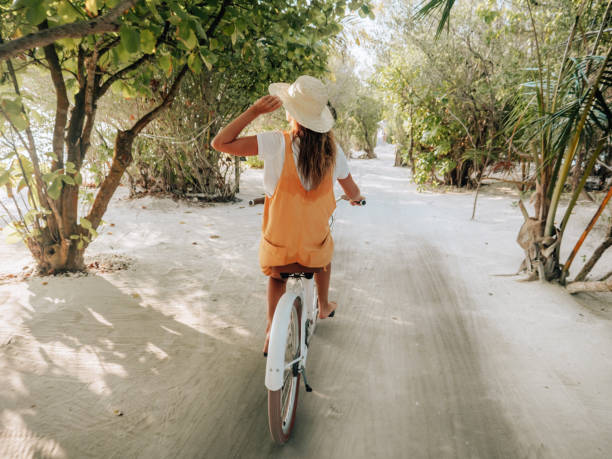 istock Young woman riding bicycle on white sand island 1327305469