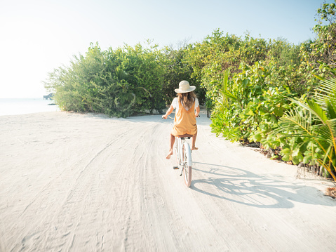 Tropical vacations young woman with bicycle in the Maldives. Female enjoying bike ride on sandy island. Dreamlike destination