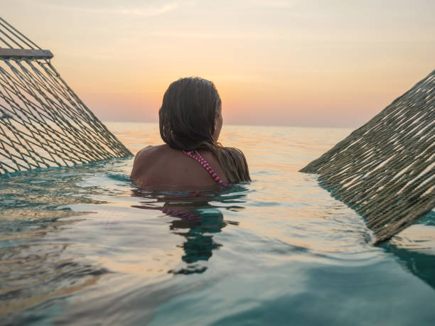Young woman watching sunset from sea hammock Young woman watching sunset from sea hammock enjoying tropical vacations in the Maldive Islands. People travel relaxation. Girl relax on hammock over sea looking at seascape beach holiday photos stock pictures, royalty-free photos & images