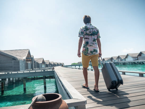 男は熱帯の目的地で木製の桟橋にトロリーを引っ張ります - travel suitcase hawaiian shirt people traveling ストックフォトと画像