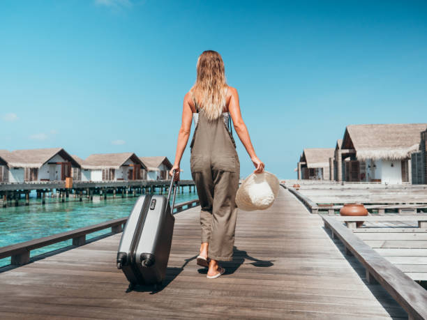 Woman pulls trolley on wooden pier in tropical destination Low angle view of woman arriving in hotel, Maldives hand luggage stock pictures, royalty-free photos & images