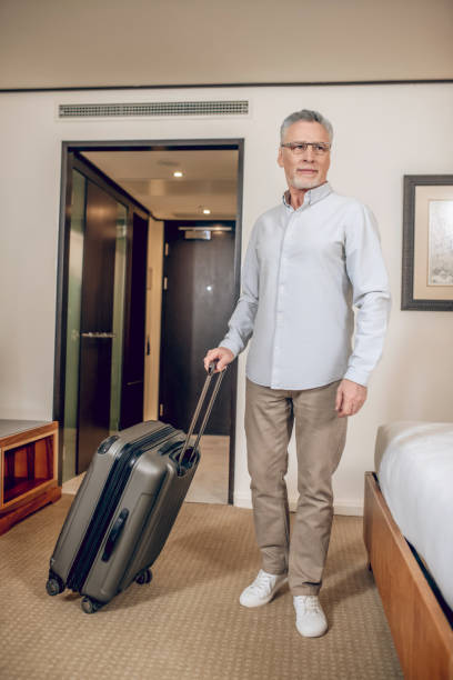 istock Gray-haired confident man with a suitcase in a hotel room 1327310050