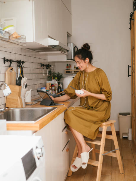 Asian freelancer working in kitchen room. Young asian woman is sitting in the kitchen eating breakfast and working on digital tablet. lifehack stock pictures, royalty-free photos & images