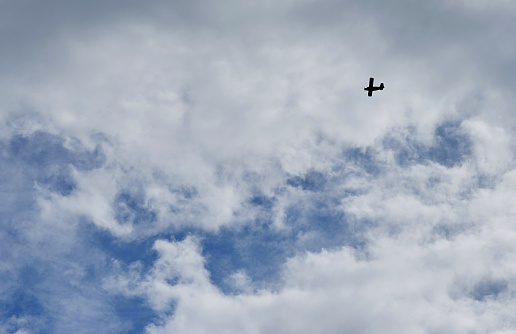 A small sports plane flies through the sky with clouds.