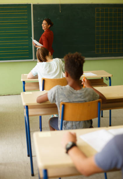 istock Teacher writing on chalk board in front of a class. 1327311689