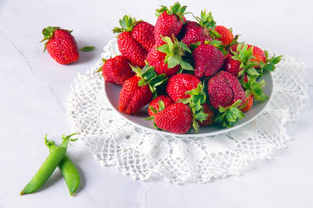 fraises rouges fraîches et gousses de pois verts sur table en marbre blanc. - doily freshness raw sweet food photos et images de collection