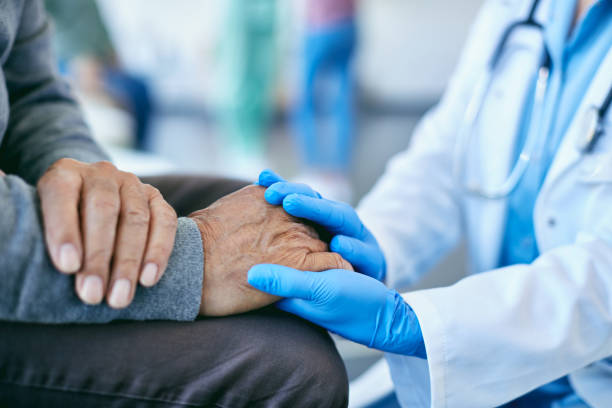 close-up of healthcare worker consoling mature patient and holding his hand at medical clinic. - holding hands human hand senior adult consoling imagens e fotografias de stock