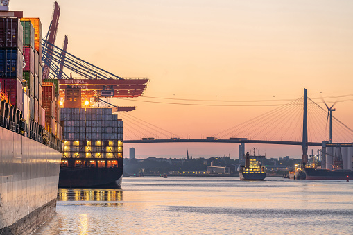 Cargo terminal in Hamburg, Europe on a nice evening.\nHuge cargo ships are ready for unloading their containers.\nBehind the famous harbor bridge of Hamburg, Germany.