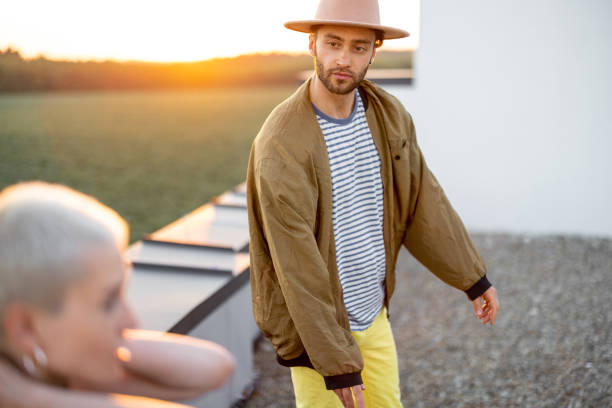 Stylish carefree man wearing coat, hanging out on the rooftop with friends at sunset