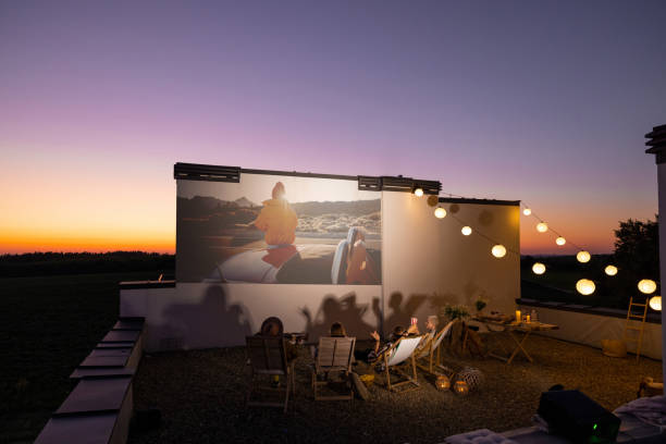 People watching movie on the rooftop terrace at sunset Small group of people watching movie on the rooftop terrace at sunset. Open air cinema concept. Romantic leisure and entertainment on the roof of a country house film screening stock pictures, royalty-free photos & images
