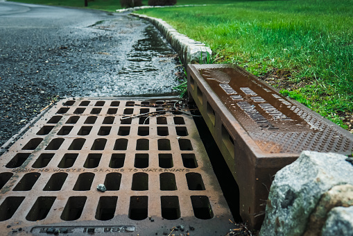 A storm drain on the side of a road reads 