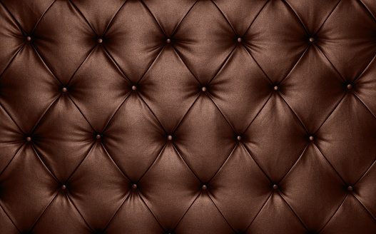 Close up background texture of dark brown capitone genuine leather, retro Chesterfield style soft tufted furniture upholstery with deep diamond pattern and buttons