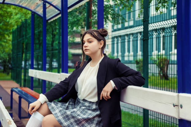 Portrait of thirteen-year-old schoolgirl in white blouse, plaid skirt and jacket at schoo Art noise film style image. Portrait of thirteen-year-old schoolgirl in white blouse, plaid skirt and jacket at school. Emotional teen girl posing looking at camera. Concept of school age and learning back to schoo stock pictures, royalty-free photos & images