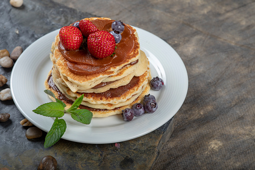 Pancakes cascaded on top of each other with a nut filling.\nTop with caramel sauce garnished with strawberries and blueberries.