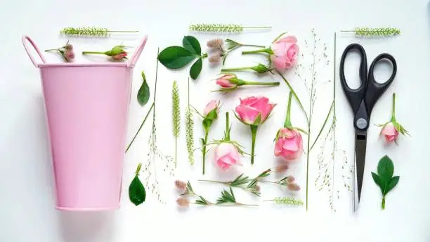 Floristic composition flat lay.Work of the florist,drawing up a flower arrangement,on a white table pink bucket,scissors, roses,flowers and herbs,top view.Floral banner.Pastel colors