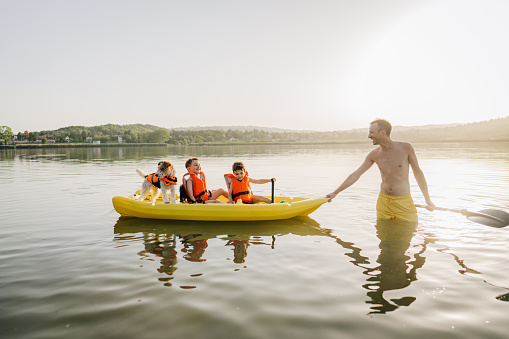 Photo of a young father, his two boys, and their dog, riding a kayak on the lake, on a hot summer day; a peaceful weekend getaway far from the city hustle.