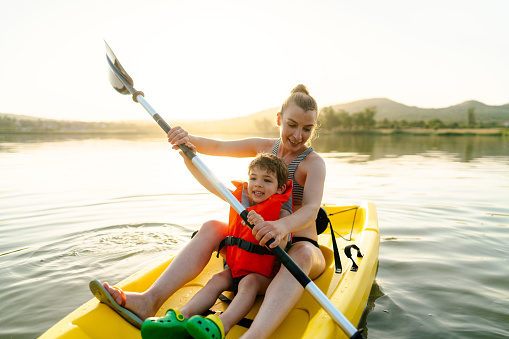 Photo of a young mother and her cute son riding a kayak on the lake, on a hot summer day; a peaceful weekend getaway far from the city hustle.