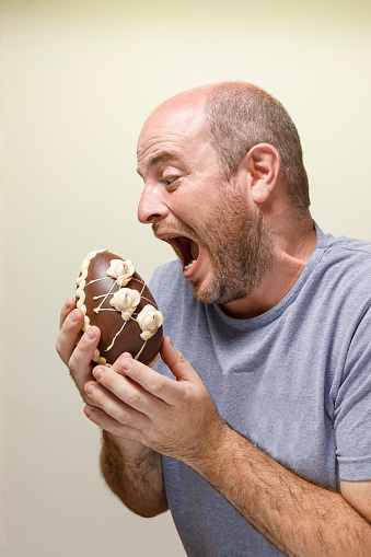 A Man eating a chocolate candy. Expression of devouring a sweet. Opening the mouth wide. Temptation. Unhealthy eating.