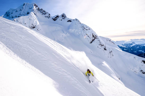 Backcountry skier descends snowy mountain ridge He sprays snow as he turns at speed, in the snowy Canadian Rockies extreme skiing stock pictures, royalty-free photos & images
