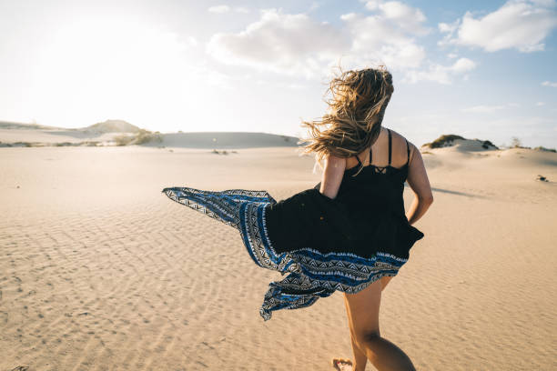 istock Young woman runs barefoot along sand dune 1327366437