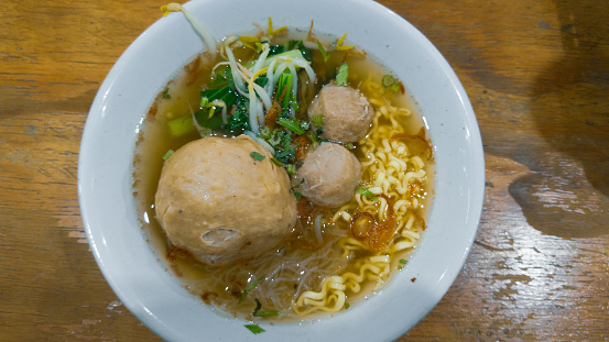 a bowl of Indonesian meatballs soup with vegetables and noodles on wooden table