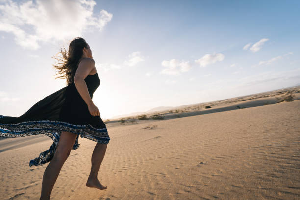 istock Young woman runs barefoot along sand dune 1327367109