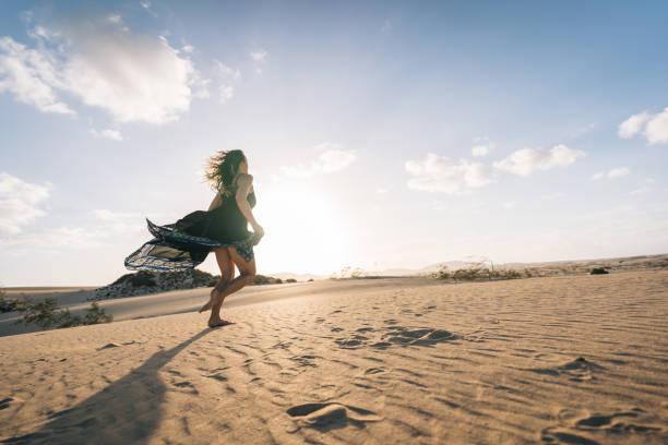 istock Young woman runs barefoot along sand dune 1327367202