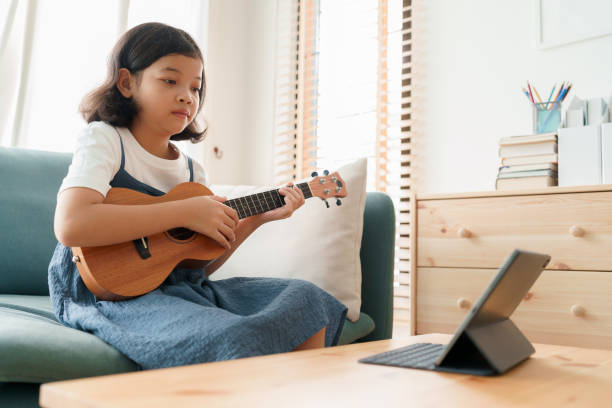 Asian little girl is practicing ukulele playing on tablet