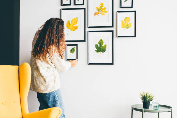 mujer colgando marco de cuadro en la pared en la casa nueva. ideas de decoración del hogar para el otoño - decorar fotografías e imágenes de stock