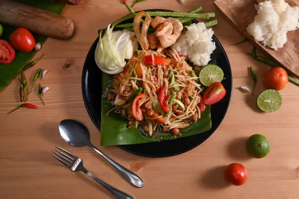 Photo of Green papaya salad with sticky rice on wooden table. Thai traditional food.