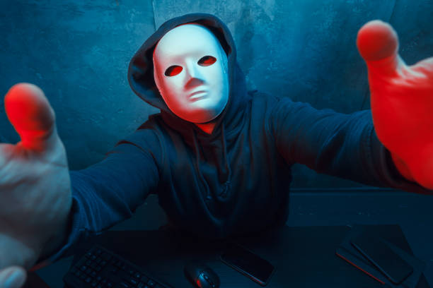 hacker anonimo che indossa la maschera facciale che lavora al computer nella stanza buia - anonymous rete di attivisti foto e immagini stock