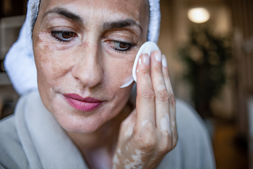 One woman, a mature woman who has cosmetic treatment at home, applies a face cream and a liquid skin preparation.