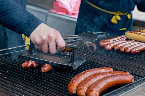 Roasting sausages on charcoal in the outdoor. The man's hand presses the sausages to the grate