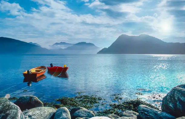 Photo of Morning mood on a Norwegian fjord with rising sun. In the foreground two colourful rowing boats