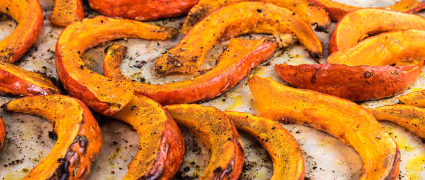 istock Baked pumpkin slices cut into slices on parchment - close-up, panoramic view 1327419782
