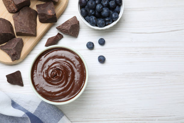 istock Delicious chocolate cream and blueberries on white wooden table, flat lay. Space for text 1327419884