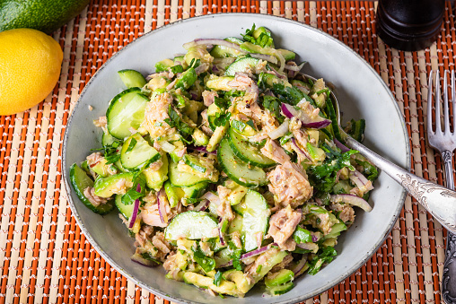Seasonal green salad with cucumbers, avocado, onions and canned tuna in a plate close-up